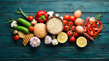 Ingredients for breakfast: Eggs, oatmeal, sausages and fresh vegetables on a blue wooden background. Top view. Free space for your text.