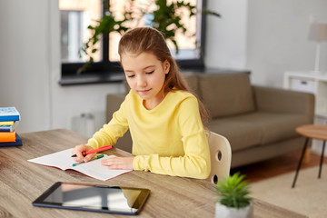 children, education and school concept - happy student girl with tablet pc computer writing to notebook at home