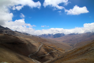 Plateau winding road, blue sky and white clouds, snowy mountains in the distance