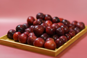Red plum fruit on wooden tray with red background.