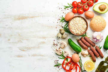 Ingredients of healthy nutrition. Cooking background: Eggs, oatmeal, sausages and fresh vegetables on a white wooden background.