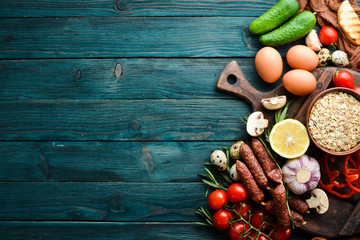 Ingredients for breakfast: Eggs, oatmeal, sausages and fresh vegetables on a blue wooden background. Top view. Free space for your text.