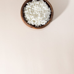 Fresh homemade cottage cheese in a wooden bowl on a beige square background with copy space, dairy product source of calcium protein vitamins, healthy diet