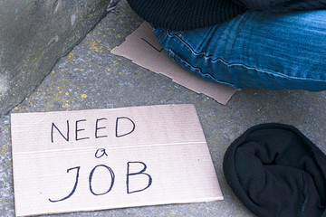 concept unemployment, poverty, job search, next to an unemployed person sitting on the ground is...