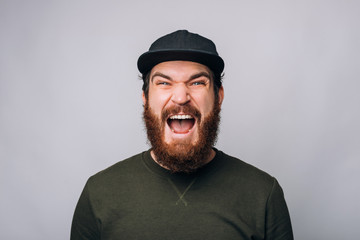 Handsome bearded man wearing a cap is screaming or shouting at the camera.