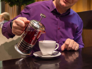 Fototapeta na wymiar a man in a colored shirt pours tea into a Cup from a French press teapot.close up. copy space