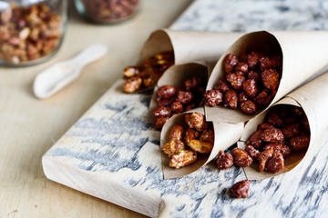 Caramelized sugared peanuts in paper envelope bags on wooden background. Selective focus