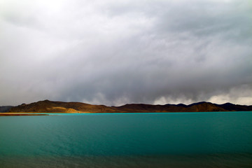 Plateau holy lake, blue-green lake water, coffee-colored distant mountains, rising water vapor and clouds