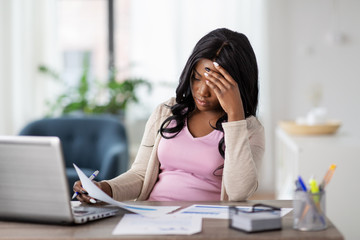 Obraz premium remote job, technology and people concept - stressed young african american woman with laptop computer and papers working at home office