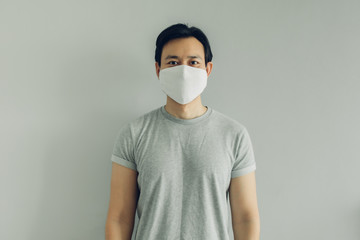 Normal face of Asian man wearing white hygienic mask in grey t-thirt with copy space.