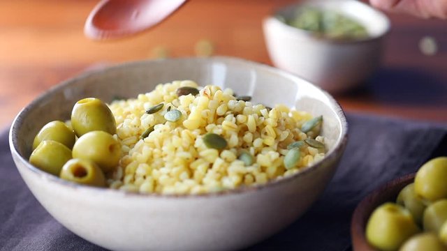 Female hand adds green olives to a freshly brewed bulgur. Healthy dinner or lunch.