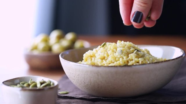 Female hand sprinkles papitas with freshly brewed bulgur. Healthy dinner or lunch.