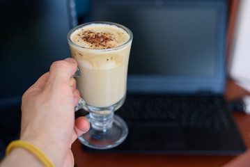 Male hand with a cup of dalgona coffee on the laptop background. The beginning of the working day
