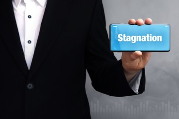 Stagnation. Geschäftsmann im Anzug hält ein Smartphone in die Kamera. Der Begriff Stagnation steht auf dem Handy. Konzept für Business, Finanzen, Statistik, Analyse, Wirtschaft