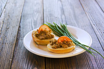 Homemade pate of pig or chicken liver on wheat buns on a white ceramic plate on brown wooden background. Pate recipes.