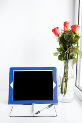 tablet, notepad and a bouquet of flowers on the desktop by the window, place for text 