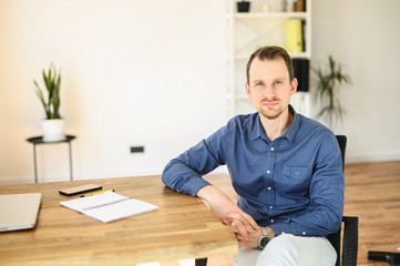Fototapeta na wymiar Office work. Portrait of young confident businessman in smart casual wear, a guy sits at the table and looks at camera with a smile