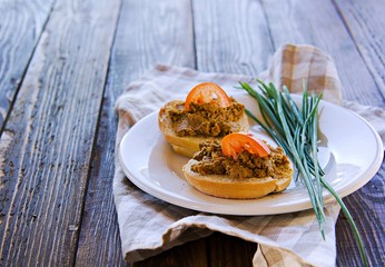 Homemade pate of pig or chicken liver on wheat buns on a white ceramic plate on brown wooden background. Pate recipes.