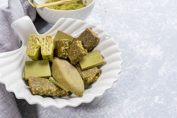 Close up plate as shell with treats containing matcha, bowl of Matcha powder,napkin on light grey background.