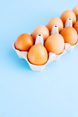 Overhead view of fresh brown chicken eggs in open egg carton box on blue background. Top view with copy space.