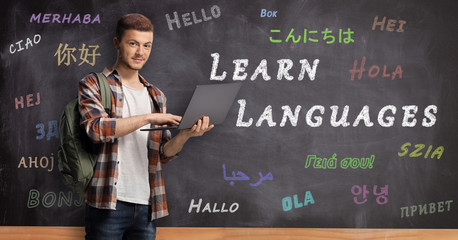 Male student with laptop standing in front of a blackboard with text learn languages