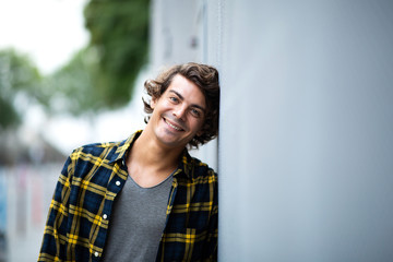 cool young man leaning against wall outside and smiling