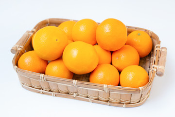 Raw oranges in wooden basket isolated on white background. Basket sewing with straw. Close-up angled view. Citrus fruit and healthy food concept