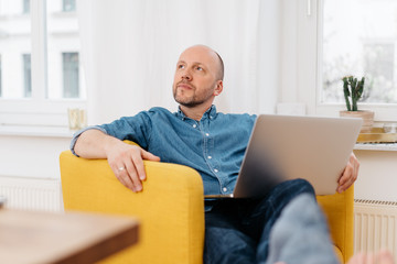 Thoughtful man relaxing with his laptop at home