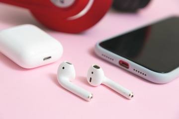 Close-up Wireless earphones, mobile phone and charging case on pink background.