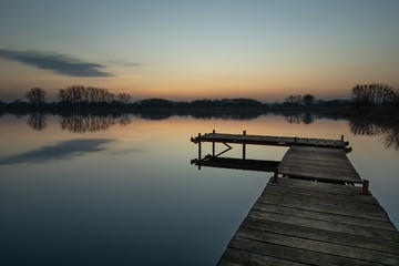 Wooden fishing pier on a calm lake, sky after sunset and one cloud