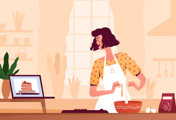 A young woman watches a recipe video on a laptop and prepares pancakes at home in the kitchen at home. The concept of home cooking and search for a recipe on the Internet