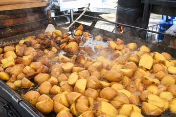 Potato wedges in skin roasting frying in large pan during hotel brunch buffet outside outdoor