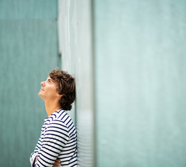 Fototapeta premium Side of handsome young man leaning against green wall looking up