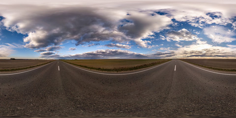 Fototapeta na wymiar Full spherical seamless panorama 360 degrees angle view on no traffic asphalt road among fields in evening before sunset with cloudy sky. 360 panorama in equirectangular projection, VR AR content
