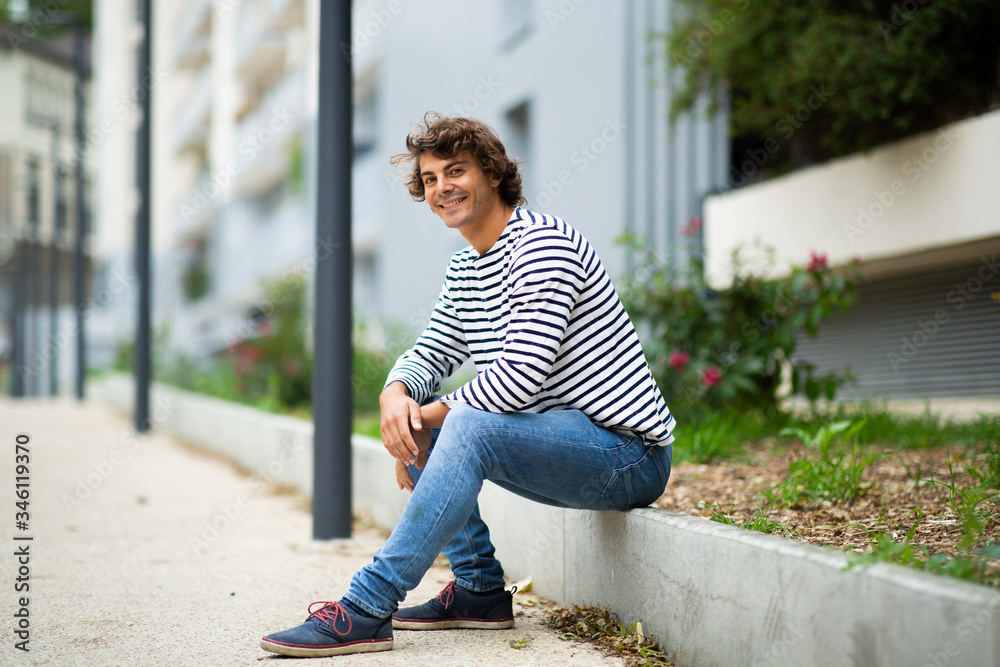 Wall mural side of smiling handsome young man sitting outside in city