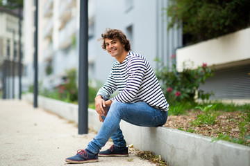 Side of smiling handsome young man sitting outside in city