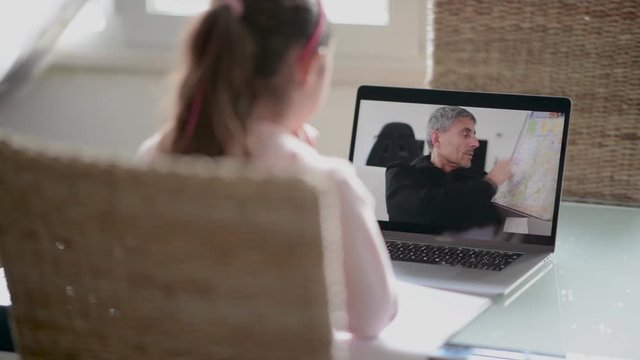 Young girl of primary school studying at home with internet chat with teacher preparing for exam. School student learning online, watch webinar make notes looking at laptop, distance education