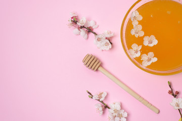 honey in a plate with a spoon and cherry flowers on a pink background. natural ingredient for skin care