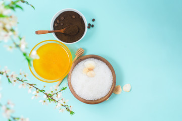 Spa products for home body care for cellulite and acne. sea salt, coffee scrub, honey in plates on a blue background and a flower branch. spring composition of organic ingredients