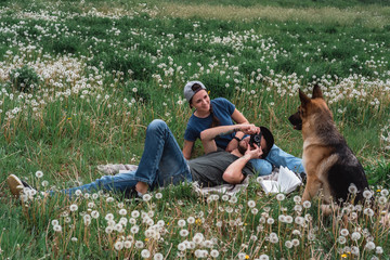 Family photo shoot with a dog in a field of dandelions. A guy, a girl and a German shepherd in nature.