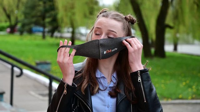 Video portrait of a young girl putting on a medical mask outdoors in the city in spring