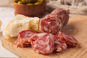 Sliced salami, bread, olives and cutting board on a white background, seen from the front