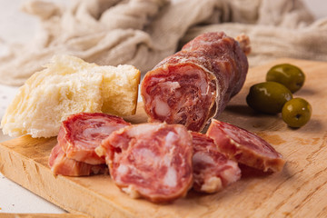 Sliced salami, bread and cutting board on a white background, seen from the front.