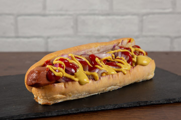 Hot Dog with mustard and ketchup on slate plate and white brick wall