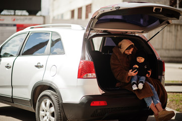 Young mother and child sitting in the trunk of a car and looking at mobile phone. Safety driving concept.