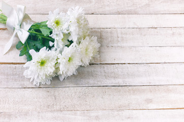 white chrysanthemum bouquet with silk ribbon lies on white wooden table