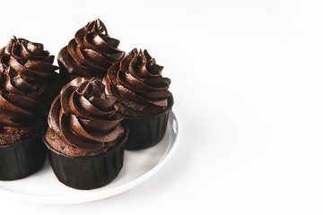 Delicious chocolate cupcakes with chocolate icing and sprinkled gold sparkles on white porcelain plate on isolated white background. Mockup for your design. Close-up. Place for text.