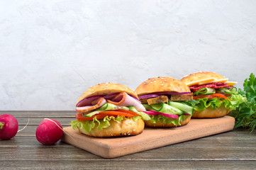 Different burgers on a wooden board. Homemade bun with ham or meat or salami, vegetables, herbs. Sandwiches for lunch.