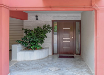 Fototapeta na wymiar dark pink portico of apartment building entrance covered with white marble, potted plants and dark wood door