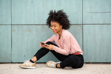 Portrait young african american woman sitting on floor outside looking at cellphone